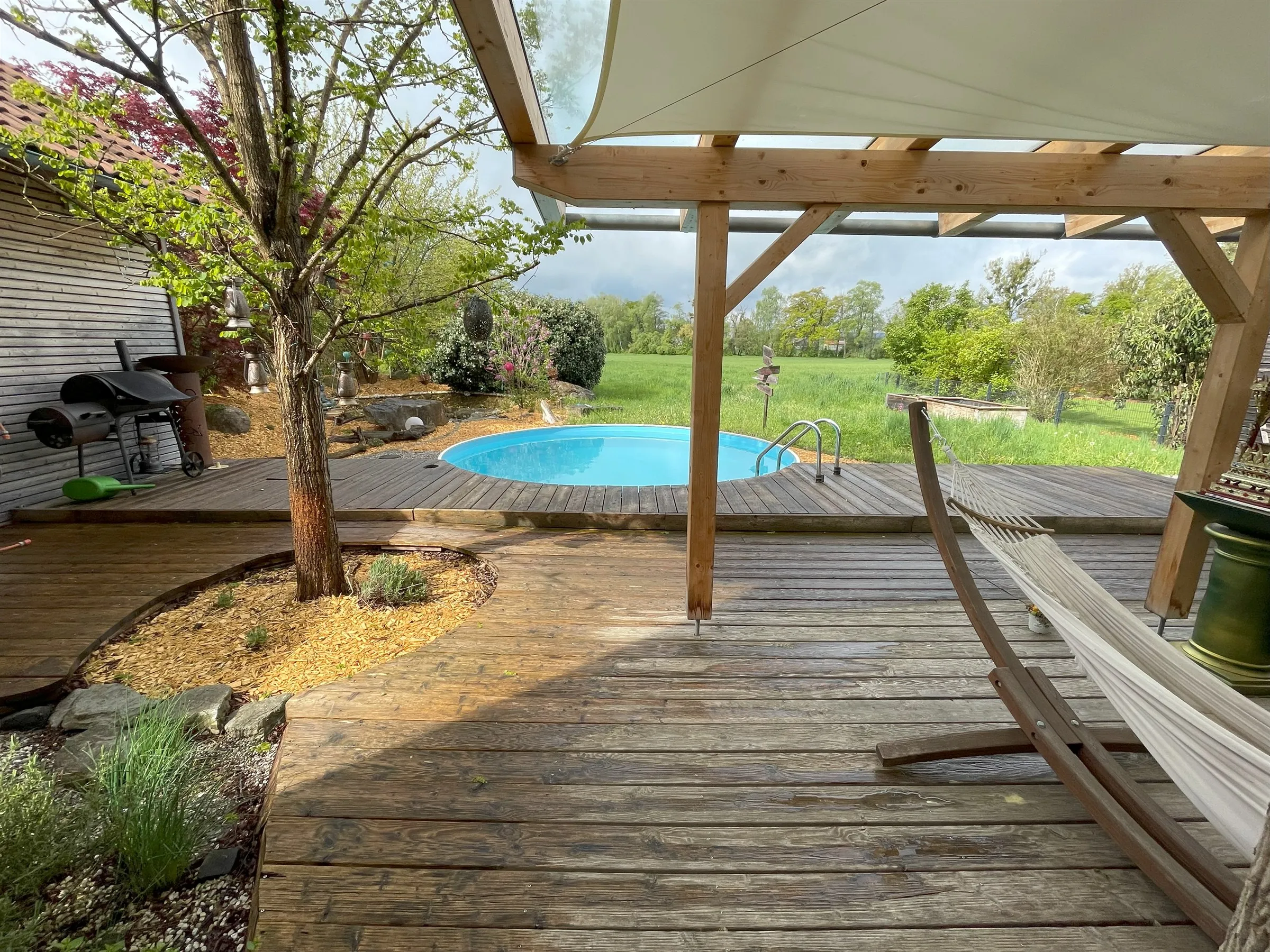 Holzterrasse mit Pergola und Pool, freier Blick über die angrenzende Wiese